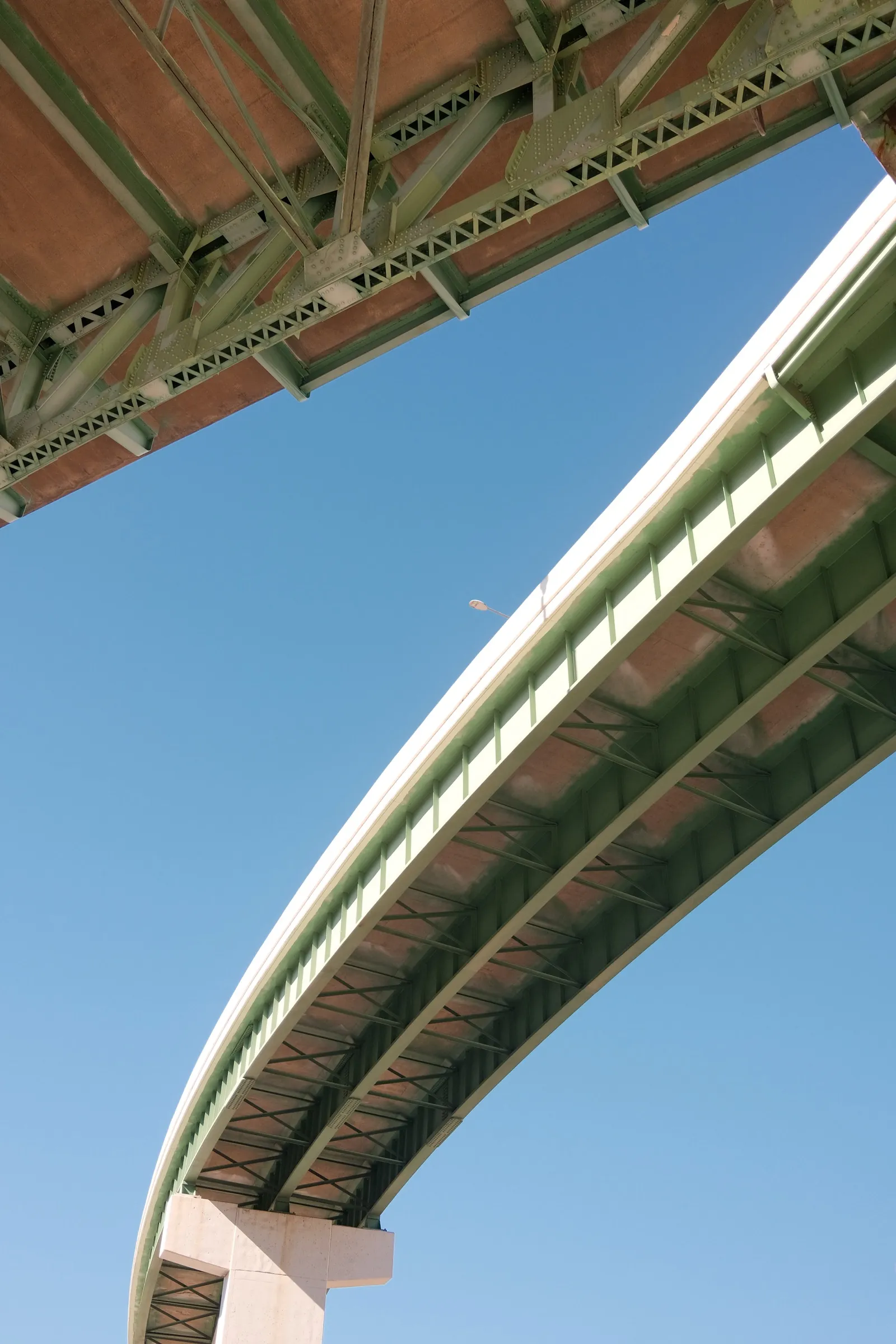 Curved bridge from below with orange underside and teal sky