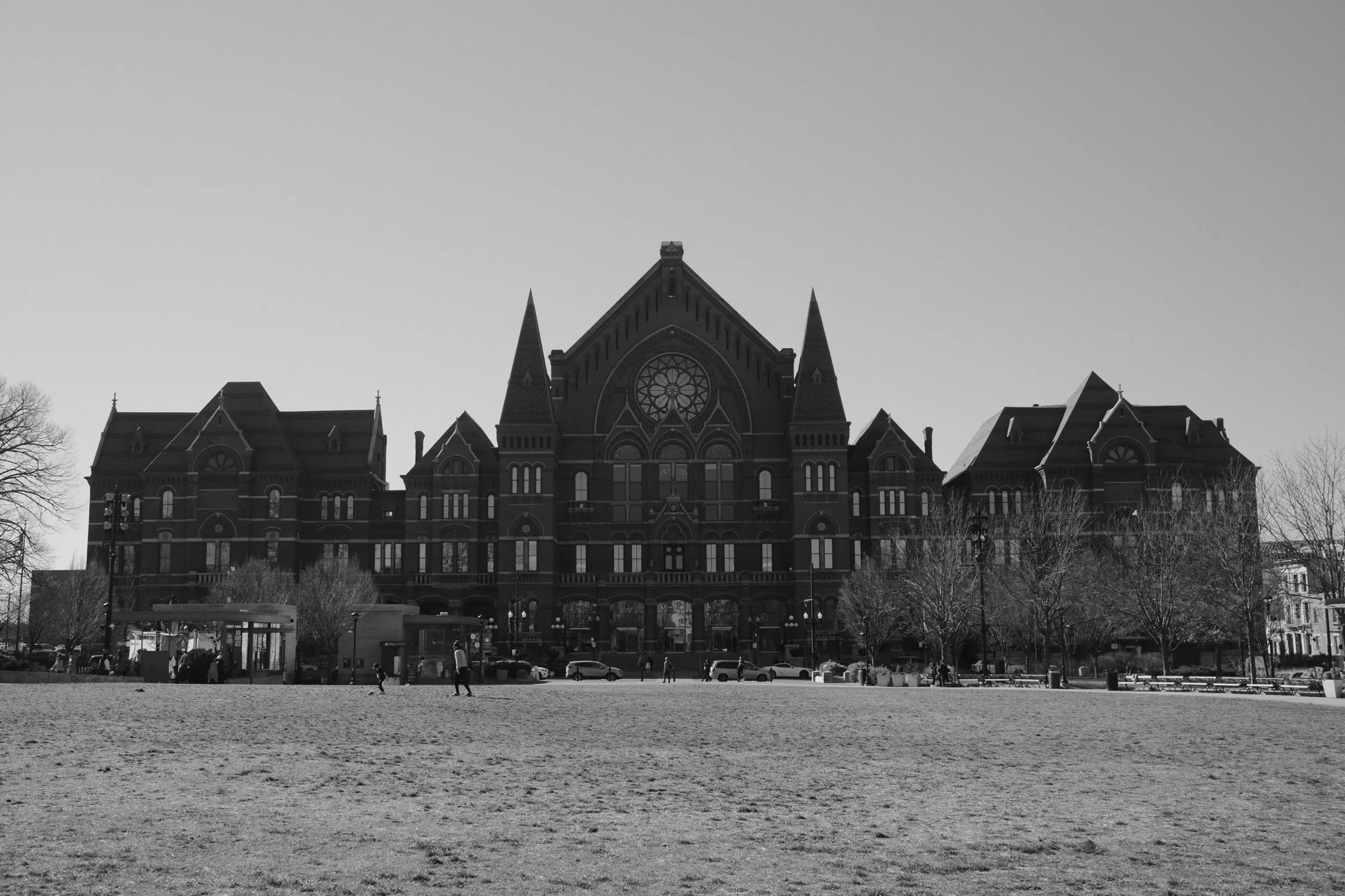 Brick Romanesque Music Hall facade with rose window seen across an open lawn, black and white