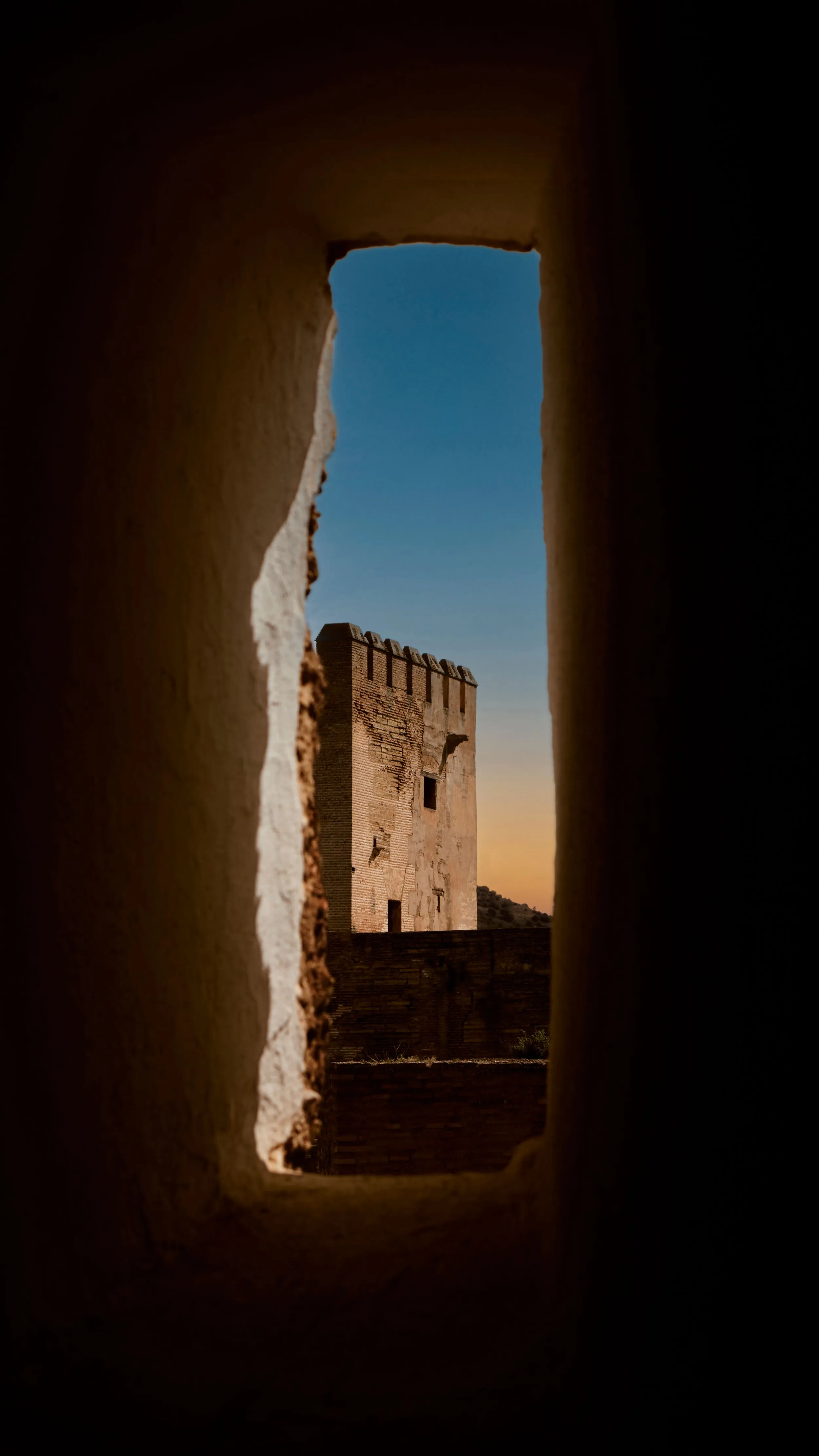 Alhambra brick tower framed through a narrow slit window at dusk, Granada