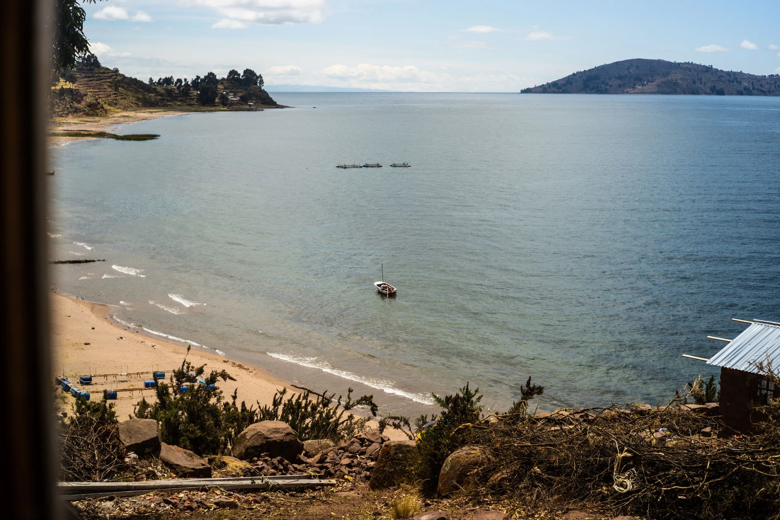 Sandy Lake Titicaca cove with moored boats, terraced hillside and distant island