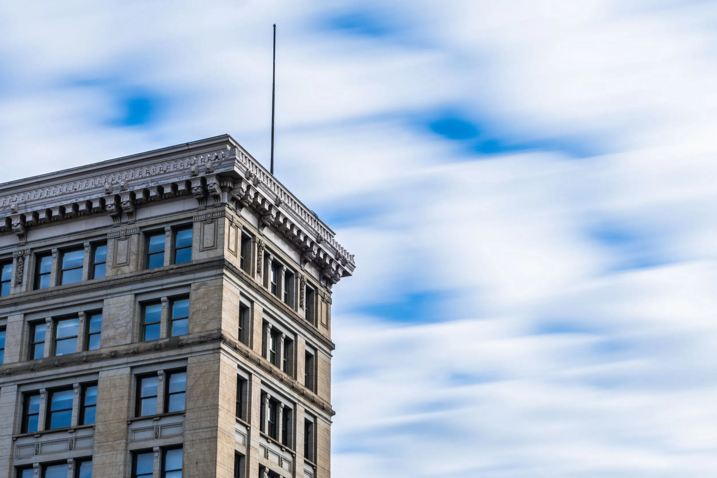 Ornate cornice of a historic stone office building against streaked cloudy sky